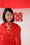 A bride wearing a red silk dress looks at the camera