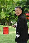 Man in traditional clothing, standing in park holding Chinese lantern