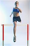 Woman running and jumping over hurdle