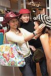 Women shopping, trying on hats, one woman adjusting hat for her friend