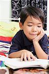 Boy lying on bed, hand on chin, reading a book