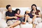 Family of four on sofa, sister tickling brother