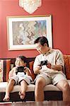 Father and son sitting side by side on sofa, playing video game