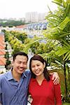 Couple standing on balcony, smiling at camera, portrait