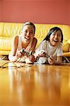 Two sisters lying on floor playing video games, smiling