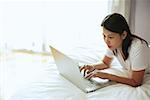 Woman lying on bed, using laptop