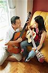Father and daughter holding guitars, sitting face to face