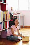 Girl sitting cross-legged on floor, holding book, looking at camera