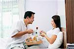 Couple in bedroom, breakfast tray between them