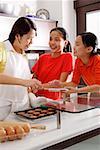 Mother and two daughters in kitchen, with tray of cookies