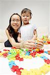 Mère et fille regardant la caméra, pièces de jouets devant eux