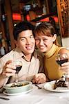 Couple in restaurant, smiling at camera, holding wine glasses
