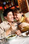 Couple in restaurant, sitting cheek to cheek, holding wine glasses