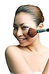 Woman applying blusher with make- up brush, smiling at camera