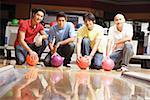 Four men crouching in bowling alley, holding bowling balls