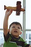 Young boy holding toy airplane, looking up
