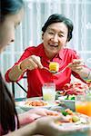 Grandmother and granddaughter at dining table, eating