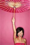 Woman holding pink umbrella, standing against pink background