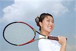 Jeune femme tenant une raquette de tennis par-dessus l'épaule, souriant à la caméra