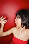 Woman in red tube tope holding red apple, mouth open
