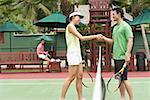 Man and woman shaking hands across tennis court