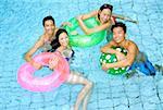 Couples in swimming pool with floats looking at camera