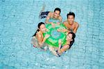 Young adults in swimming pool holding on to inflatable ring