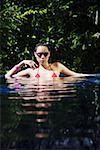 Woman sitting in swimming pool, wearing sunglasses