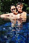 Couple sitting in swimming pool, smiling at camera