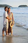 Couple debout sur la plage, eau profonde en cheville, regardant la caméra