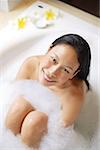Woman sitting in bathtub, smiling up at camera