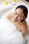 Femme assise dans la baignoire, recouvert de mousse de savon, souriant vers le haut à la caméra
