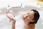 Woman in bathtub, blowing soap suds