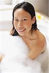 Femme dans la baignoire, recouvert de mousse de savon, souriant à la caméra