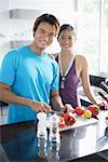 Couple standing in kitchen, looking at camera, man holding knife, chopping vegetables