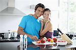 Couple standing in kitchen, looking at camera, woman embracing man