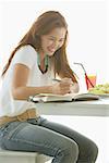 One woman sitting at table, writing in notebook, smiling