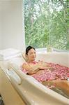 Woman lying in bath tub, flowers floating in water