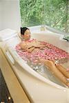 Woman taking a bath, flowers floating in water