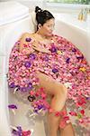 Woman in bathtub, surrounded by flowers, looking at camera