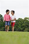 Two girls on grass, walking, side by side