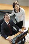 Businessman and woman in office cubicle, looking up at camera