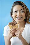 Woman holding bar of chocolate, smiling, looking away