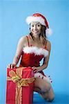 Woman in Santa hat, crouching next to gift box