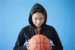 Woman wearing hooded shirt, holding basketball, looking at camera