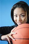 Woman wearing hooded shirt, holding basketball, smiling
