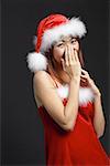 Woman wearing Santa hat and red dress, hand covering mouth