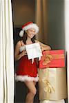 Woman in Santa hat and red dress holding gift box, smiling at camera