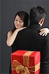 Man holding gift behind his back, woman embracing him