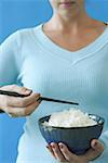 Woman holding bowl of rice and chopstick, cropped image